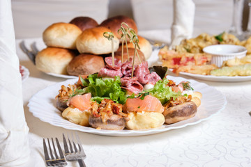 stuffed champignons, appetizer with salmon and salami on a white plate on a festive served table