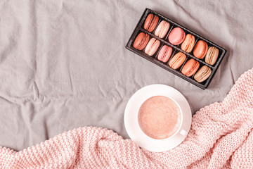 Bed with pink knitted plaid, coffee and macaroons.