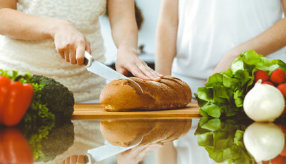 Closeup of human hands cooking in kitchen. Mother and daughter or two female friends cutting bread for dinner. Friendship, family and lifestyle concepts