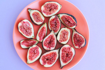 Ripe cutted figs on coral plate on violet background.
