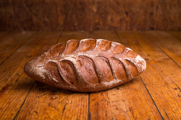 Whole grain black bread with bran on a wooden table. Loaf of bread with flour on a dark background