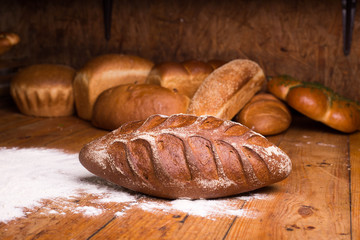 Whole grain black bread with bran on a wooden table with different breads on the background. Loaf of bread with flour on a dark background
