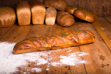 Delicious baguette with herbs on a wooden table with different breads on the background. Loaf of...