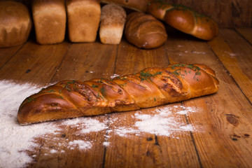 Delicious baguette with herbs on a wooden table with different breads on the background. Loaf of bread with flour on a dark background