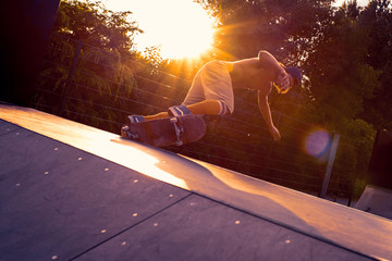 Skateboarder doing a trick over the ramp in a skate park in sunset