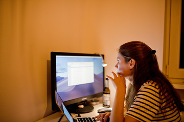 Frau denkt über ein Projekt nach und sitzt vor ihrem Laptop und Monitor