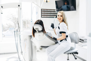 Pretty young female dentist making examination and treatment for young female patient in dental clinic.