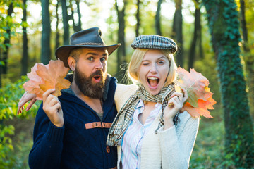 Fashion autumn portrait woman and man with yellow maple leaves on nature background. Autumn and leaf fall Dreams. Hello Autumn. Autumn love story - portrait funny couple in love - winking.