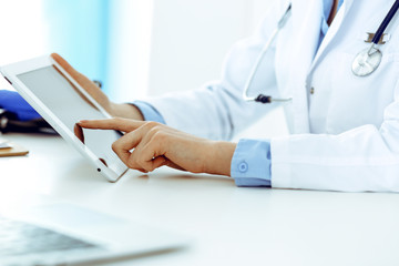 Doctor working table. Woman physician using tablet computer while sitting in hospital office close-up. Healthcare, insurance and medicine concept