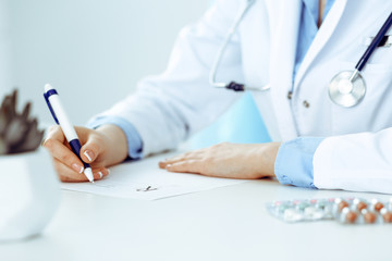 Female doctor filling up prescription form while sitting at the desk in hospital closeup. Healthcare, insurance and excellent service in medicine concept