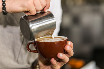 Closeup Barista in preparing proper cappuccino pouring milk froth in a cup