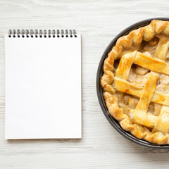 Homemade apple pie, blank notepad on a white wooden background, view from above. Flat lay, overhead, top view.