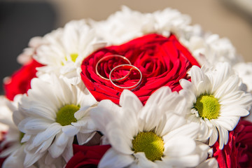 Wedding rings are on the bride's bouquet. Wedding bouquet of white daisies and red roses. Wedding background for cards and invitations.