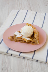 Slice of homemade apple pie with vanilla ice cream on a pink plate, side view. Close-up.