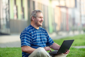 Happy man sitting on the lawn in town with laptop. Of modern urban life.