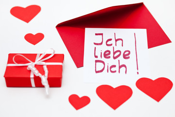 Red gift box and a love message (in German) with red envelope on a white background, decorated with...
