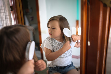 funny girl child combing hair in front of mirror
