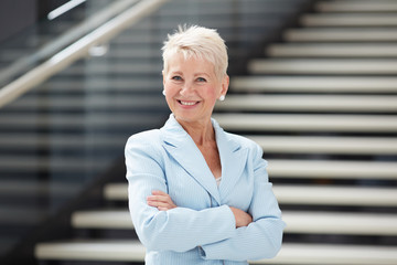 Portrait of cheerful attractive business lady in blue jacket standing with crossed arms in lobby