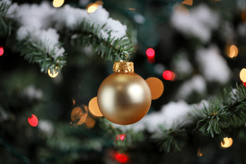 Traditional artificial Christmas tree with gold ball ornament with glowing lights and snow in...