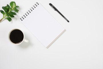 Flat lay, top view office table white desk. Workspace with notepad, pen, green leaf, and coffee cup on white background.