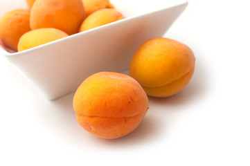 Closeup of organic apricots in a white bowl on white background