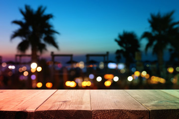 Image of wooden table in front of abstract blurred tropical palms at sunset lights background
