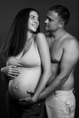Young pregnant couple hugging and smiling. Love and tenderness. Waiting for a miracle. Black and white portrait. Vertical.