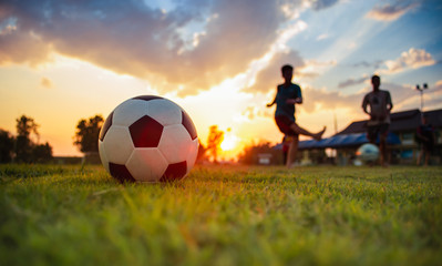 Action sport outdoors of kids having fun playing soccer football for exercise in community rural area under the twilight sunset sky. Fresh silhouette and vibrant image with anonymous people.