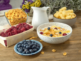Breakfast.Corn sticks ,and cereal with milk.Raspberries and blueberries.On the background colors