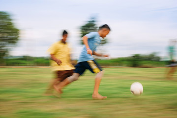 Speed motion blur picture of kids having fun playing soccer football for exercise in community rural area. Concept for sport background with anonymous people.