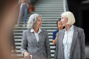 Positive mature multi-ethnic business ladies in jackets travelling together: they talking while...