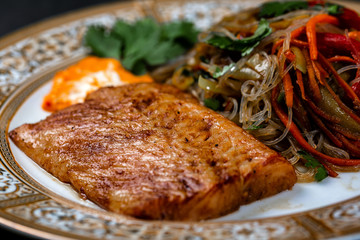 Grilled halibut steak with vegetables - sweet peppers, carrots, cilantro, on a dark background