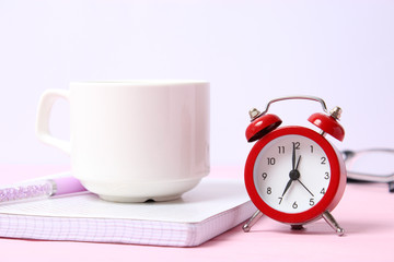 alarm clock on a colored background, a cup of coffee and stationery