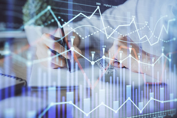 Financial forex graph displayed on hands taking notes background. Concept of research. Double exposure