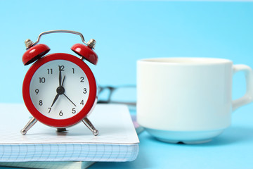 alarm clock on a colored background, a cup of coffee and stationery