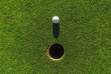 golf ball on green grass with hole and sunlight - obrazy, fototapety, plakaty