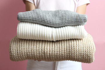 a stack of sweaters in women's hands on a colored background