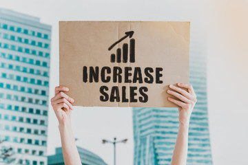 The phrase " Increase Sales " and going up icon drawn on a carton banner in men's hand. Human holds a cardboard with an inscription: Increase Sales