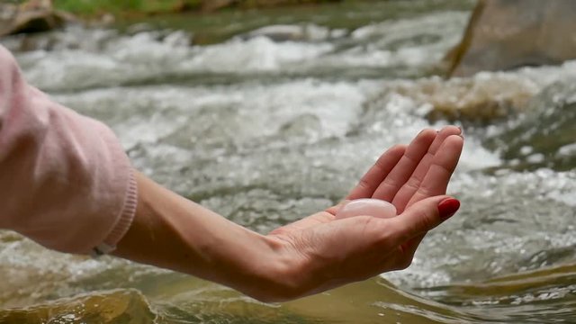 Female hand holding a rose quartz crystal yoni egg on river background. Women's health, unity with nature concepts.