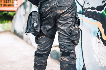 An urban man in a camouflage military pants stands next to the wall. Background from the urban part...
