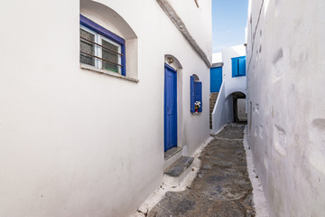 Narrow street between white traditional houses with blue door and window in town centre of Amorgos, Greece.