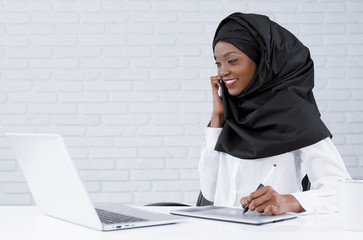 Muslim woman working in office, talking by phone.