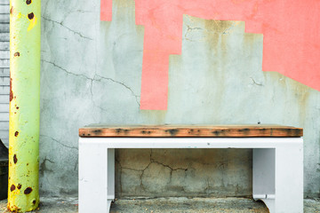 Bench on sidewalk against colorfully painted cement cracked wall.