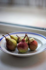 five ripe pears in a plate on the windowsill.