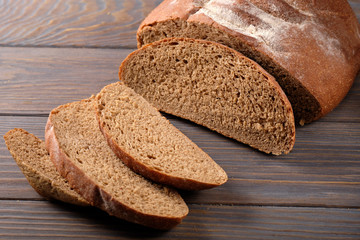 Sliced rustic bread loaf on wooden table. Dark background.