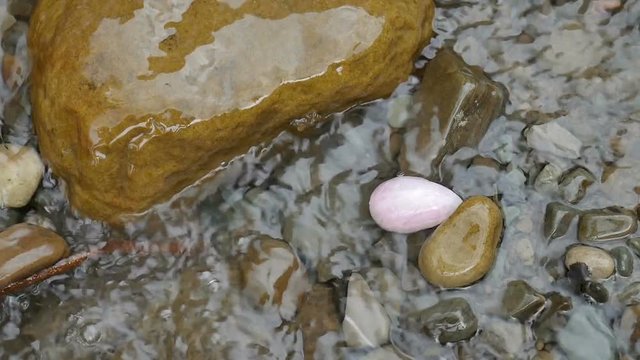 Rose quartz crystal yoni egg lying on the stones of mountains river in the water. Women's health, unity with nature concepts