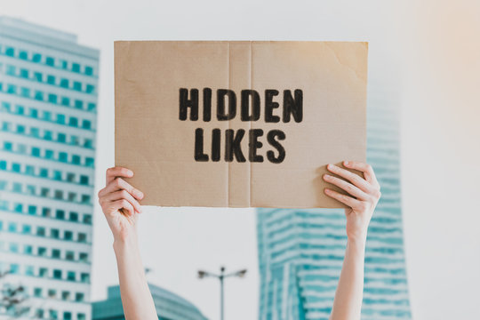 The phrase " Hidden likes " drawn on a carton banner in men's hand. Human holds a cardboard with an inscription: Hidden likes