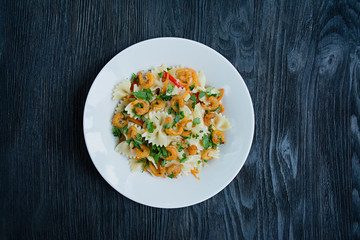Italian pasta in a sauce with shrimps on a plate, top view. Dark wooden background. Space for text.