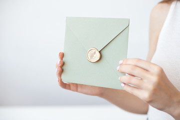 Close-up photo of female hands holding invitation envelope with a gold wax seal, a gift certificate, a postcard, wedding invitation card.