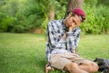 young male sleeping in the public park on the grass under the tree